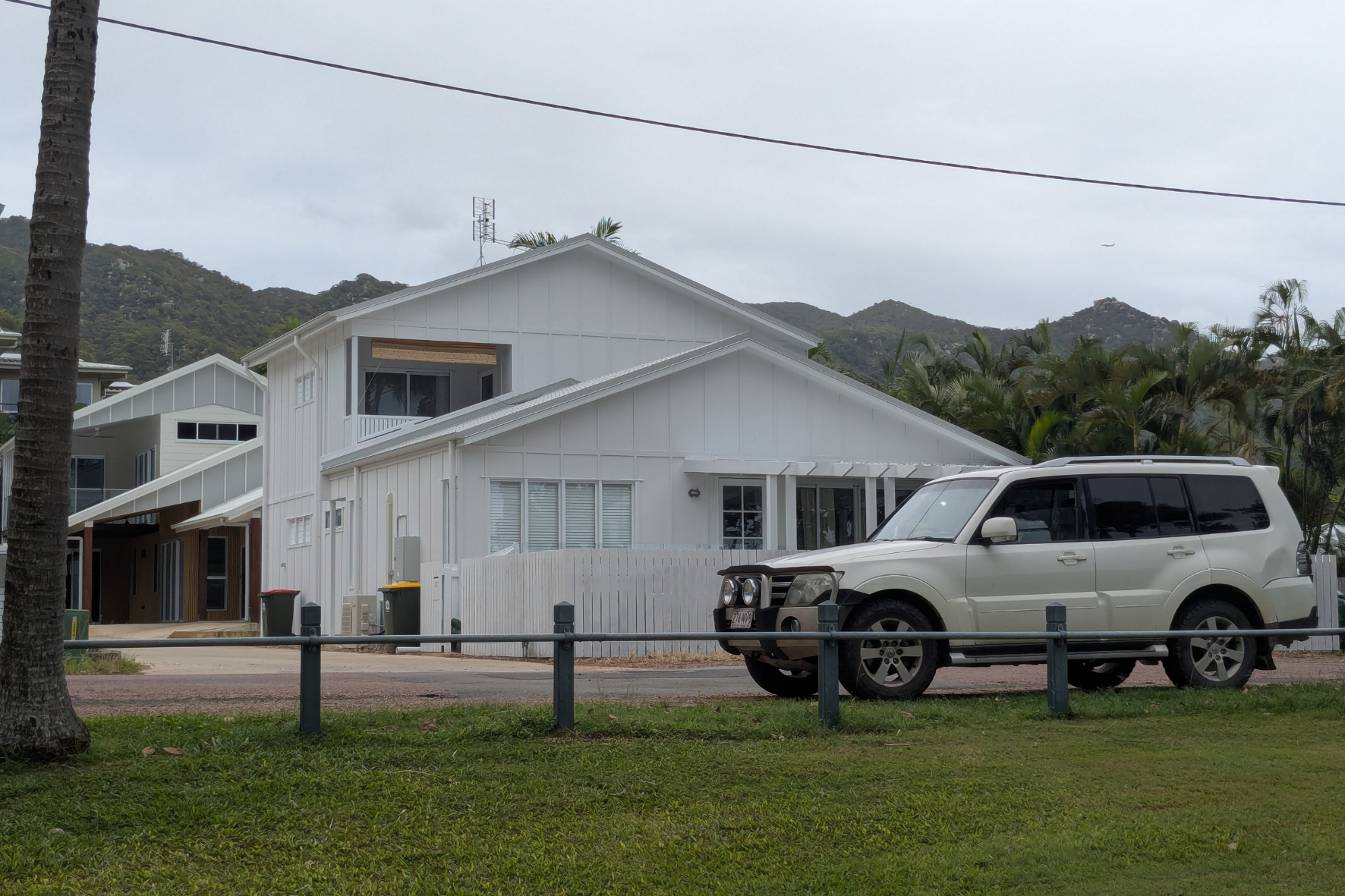 Completed two-storey white residential home with metal roof, upper balcony and Pajero parked out front, mountain backdrop