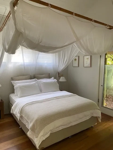 Beach House — master bedroom with white canopy, timber floors and garden outlook