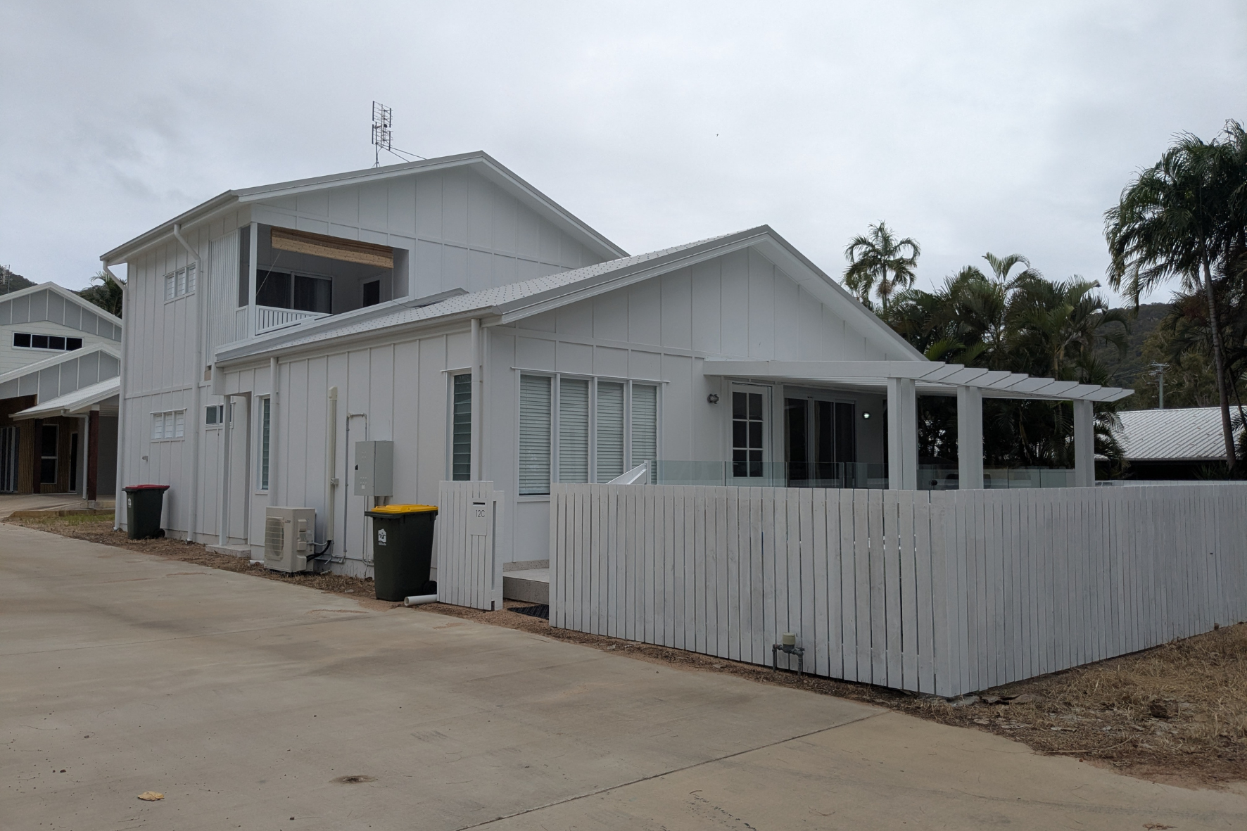 Beach House — completed side elevation showing white cladding, louvre shutters, glass balustrade and white picket fence