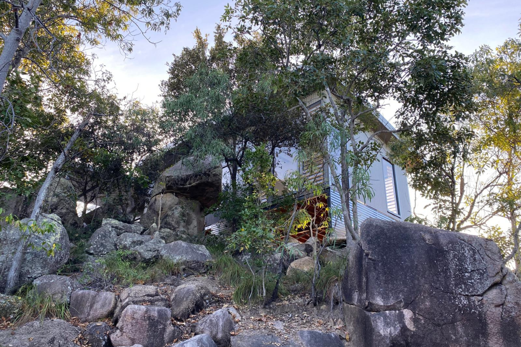 Bush Retreat — completed exterior nestled among granite boulders and native bush, corrugated cladding and louvre windows visible