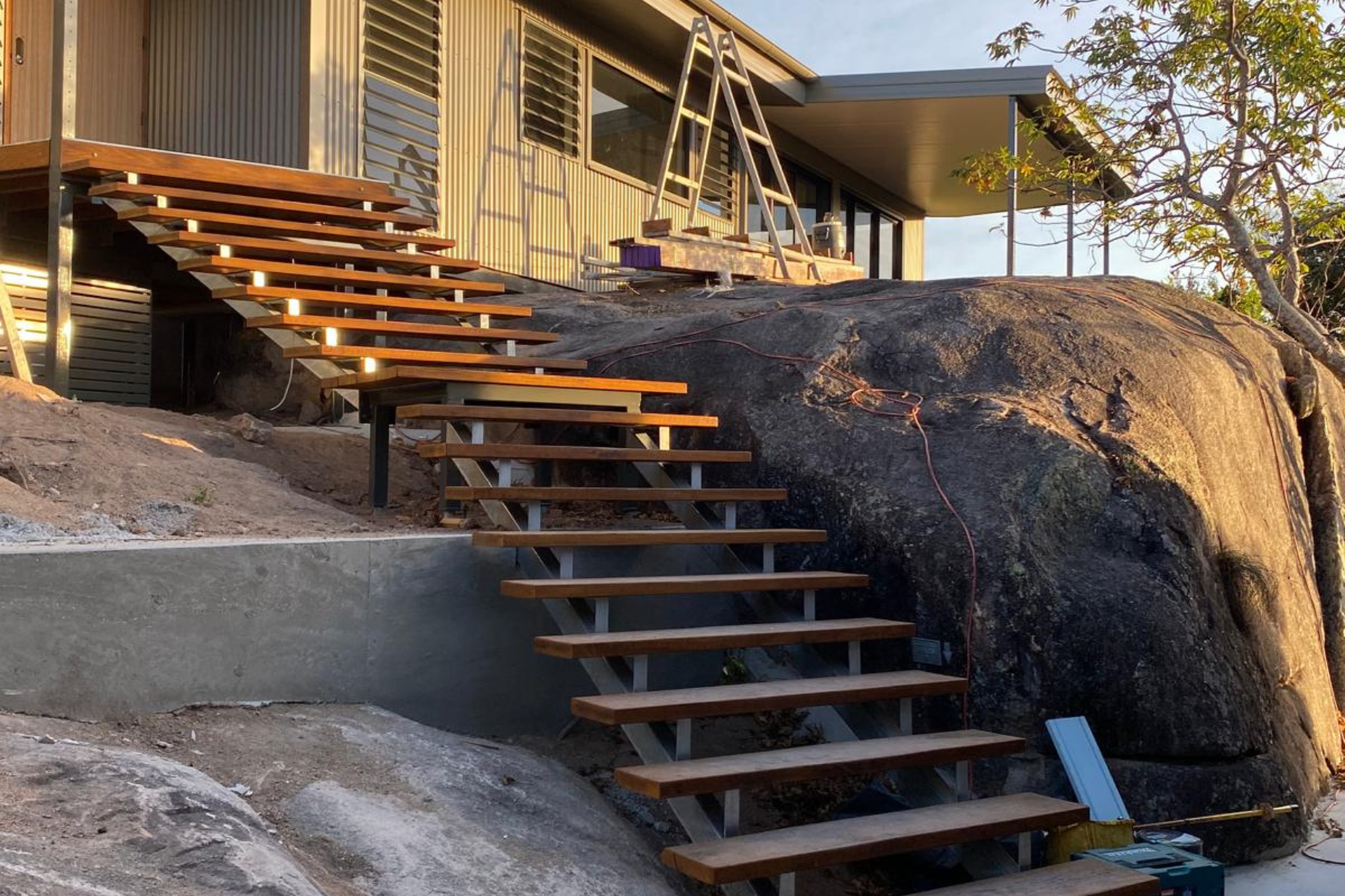 Bush Retreat — floating timber staircase with steel stringers rising beside a granite boulder to the upper deck