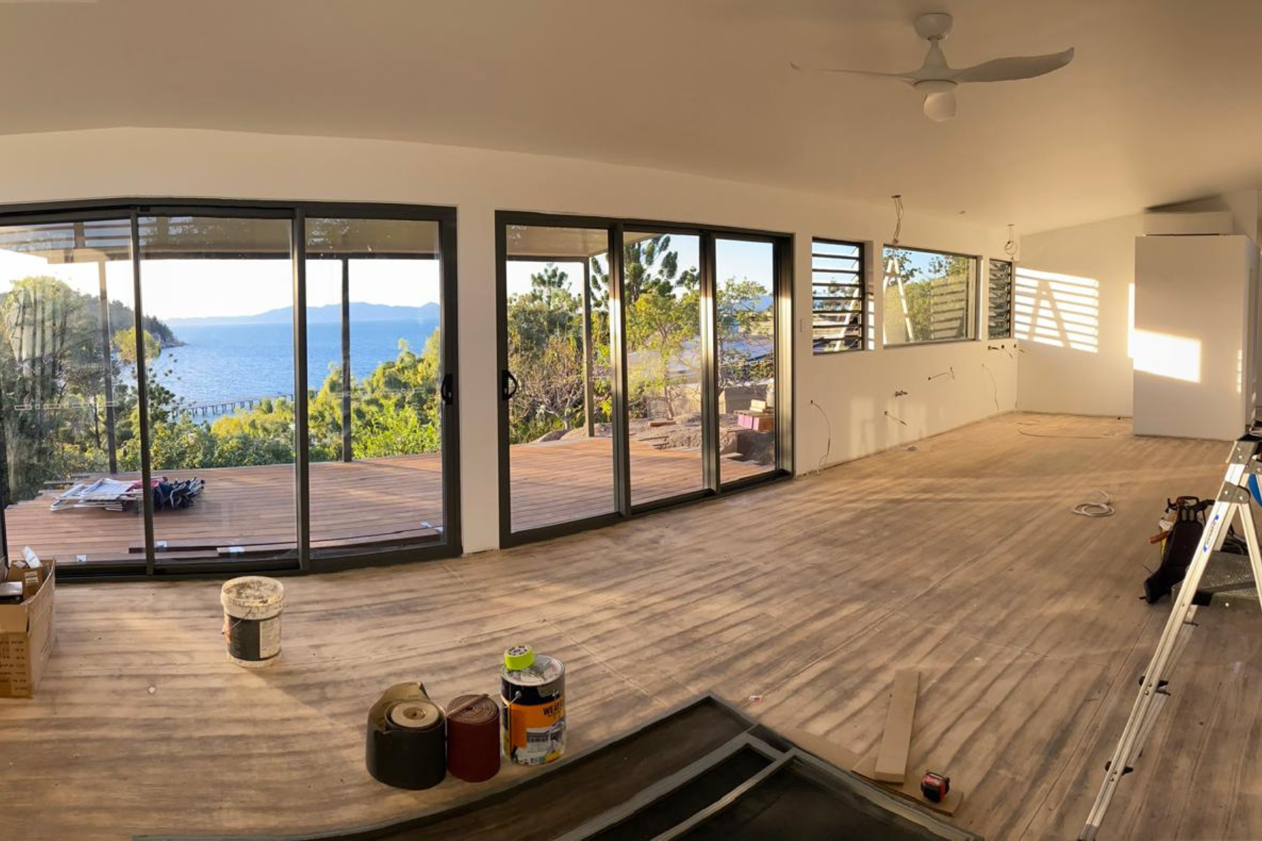 Bush Retreat — open-plan interior under fit-out with large sliding doors, louvre windows and ocean and island views