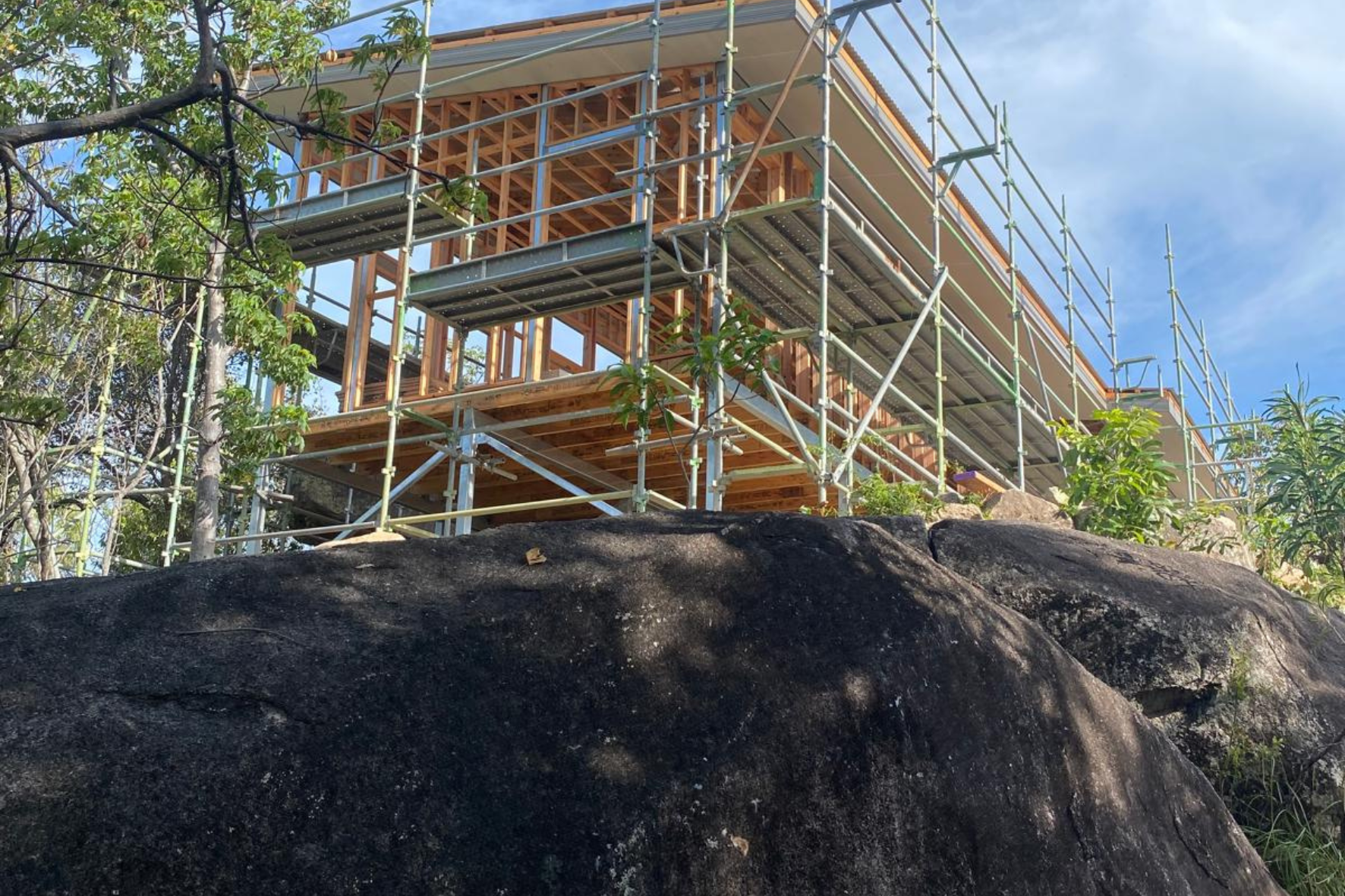 Bush Retreat — timber frame and scaffolding rising above a granite boulder during early construction phase